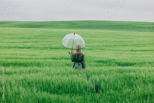 Businesswoman standing in a green wheat field with a transparent umbrella