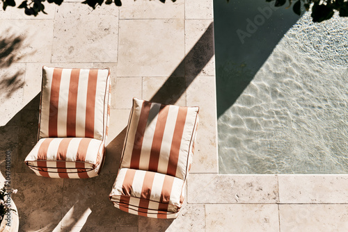Top down view of terracotta striped sun  loungers on travertine pool deck beside plunge pool with dappled sunlight.