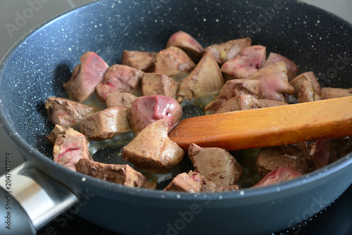 Chicken liver pieces frying in a pan with a wooden spatula close up