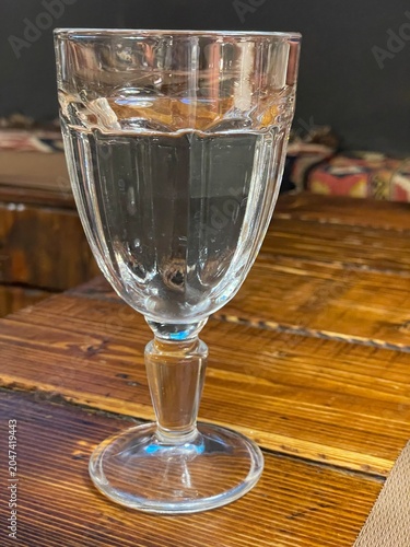 Fotografie Clear Water in Glass: A close-up shot of a stemmed glass filled with clear, refreshing water, resting on a rustic wooden surface, inviting a moment of pure hydration