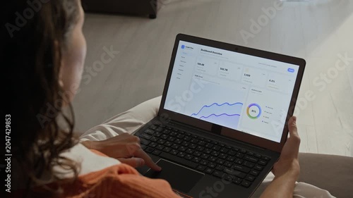 Over shoulder shot of Caucasian young adult woman analyzing business metrics and scrolling through dashboard analytics on laptop. Clip perfect for marketing campaigns about remote work and e-commerce