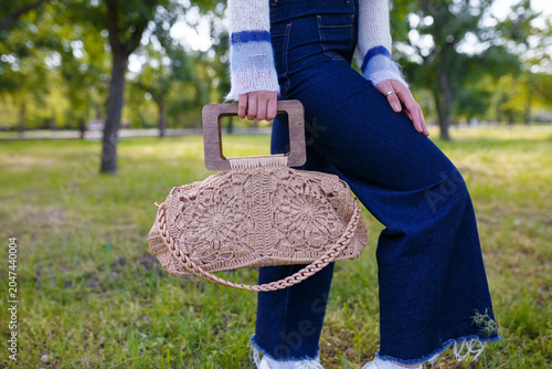 Bild auf Leinwand female hands holding whickered beige purse, legs in jeans, no face visible