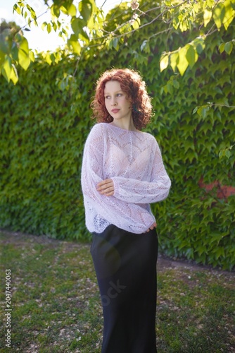 Redhead teenage girl in white knit sweater and black silk skirt posing outdoors. Knitwear
