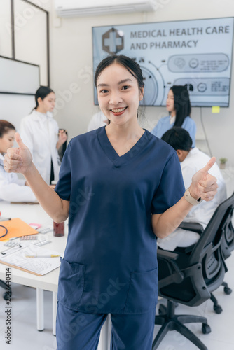 Smiling Asian woman healthcare professional in white lab coat with stethoscope holding medical chart or document in hospital meeting room.