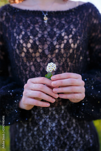 Young girl in black knitted sweater holding tiny white flower in hands. Close up shot