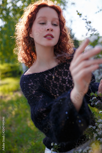 redhead teenager girl in black knitted sweater posing at white blossoming bush. Soft focused shot. Model on spring background