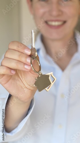 Happy woman in blue shirt smiles and offers house key to camera in successful real estate property sale or rental scene. Footage ideal for real estate agent advertising, mortgage broker content.