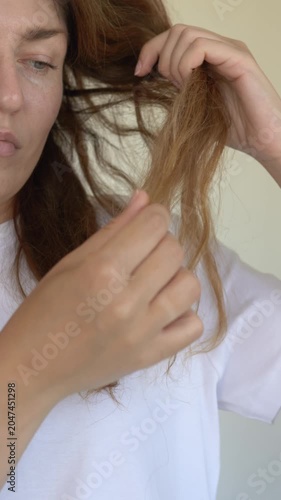 Woman pulls and examines damaged hair strand checking breakage loss and split ends in haircare concern closeup. Footage suits anti-breakage shampoo brand, trichology clinic content, hair loss beauty
