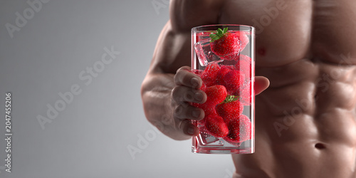 Fresh strawberries in glass with ice, held by muscular man, showcasing healthy lifestyle and fitness