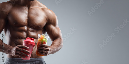 Muscular man holding protein shaker and beverage, showcasing fitness and health. Strong physique exudes confidence