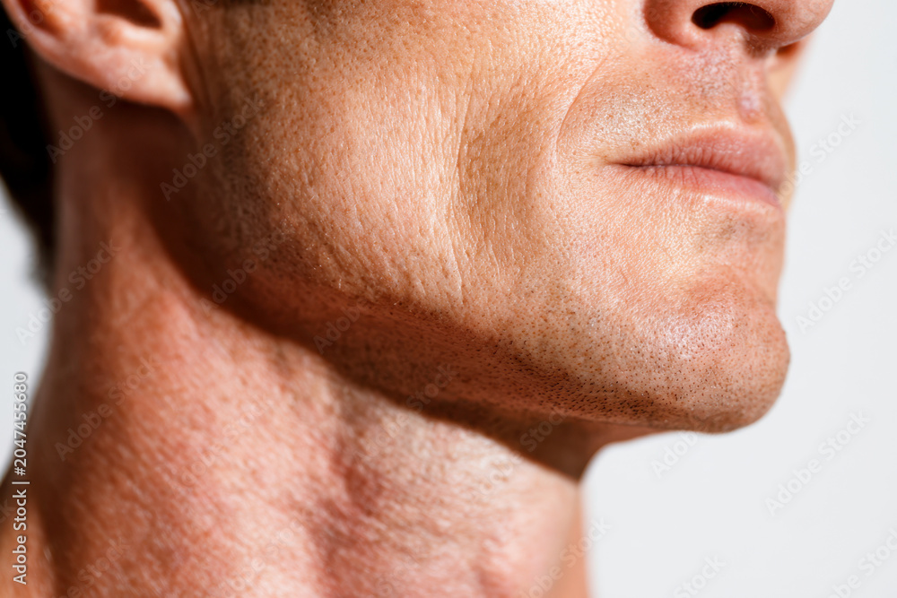 Fototapeta premium Profile view of a mature man?s lower face and neck showing natural skin texture and subtle facial hair against a plain light background