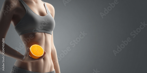 Fit woman holds fresh orange near her toned abdomen, symbolizing health and vitality. image conveys sense of wellness