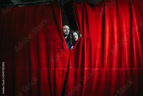 Foto Two young actors peek through a red theater curtain, watching from backstage with focused expressions