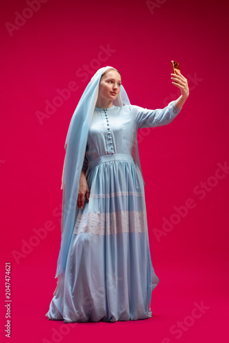 Veiled woman taking smartphone selfie on pink studio background. Concept of social media culture  digital identity  influencer content  and modern self presentation.