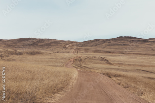 Foto Scenic winding dirt road crossing dry steppe hills on Olkhon Island, Irkutsk Obl