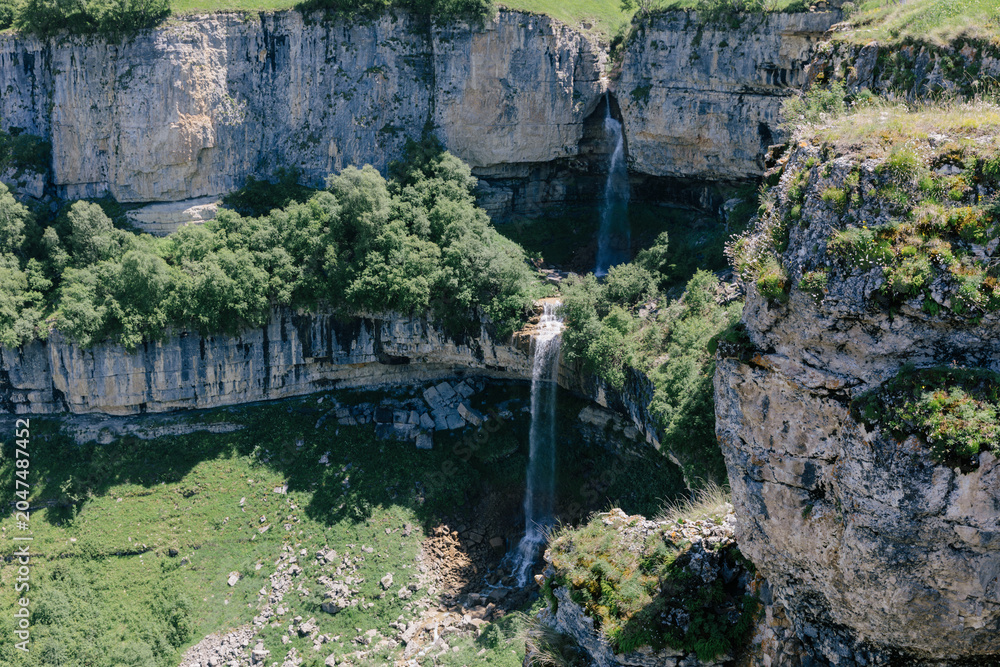 Fototapeta premium Wide landscape view of Matlas waterfalls dropping from high limestone cliffs into a green canyon near Matlas village, Khunzakh District, Dagestan, Russia
