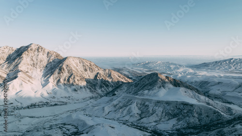 Aerial winter view of snow-covered mountains and valleys in Chunkurchak Valley near Tatyr, Chuy Region, Kyrgyzstan, with clear sky and distant ridgelines