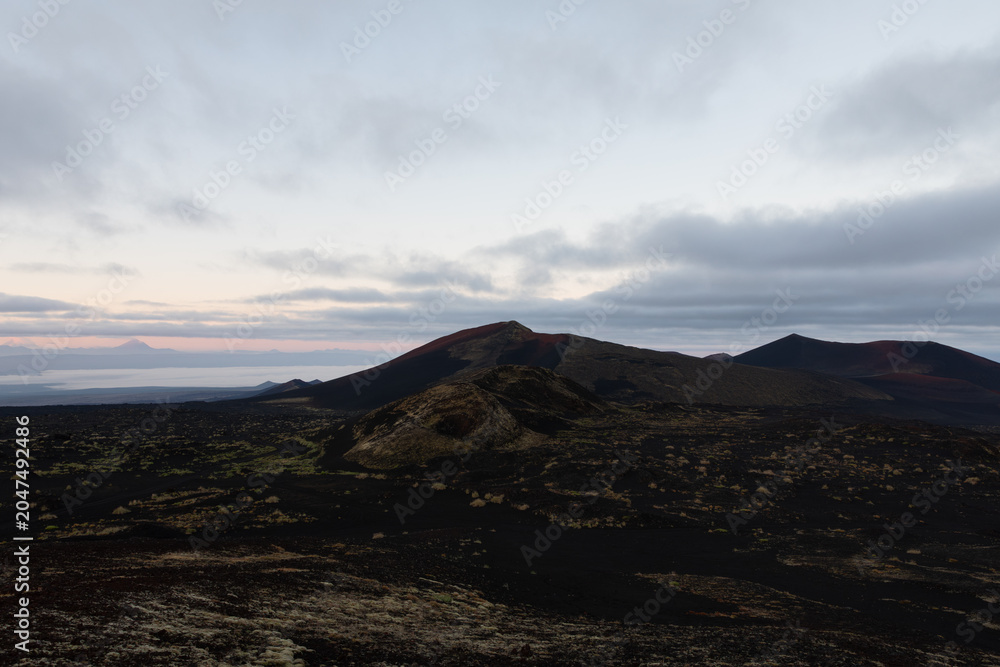 Obraz premium Wide view of Tolbachinsky Dol volcanic plateau with dark cinder cones, black lava fields and sparse moss under dramatic clouds, Kamchatka Krai, Russia