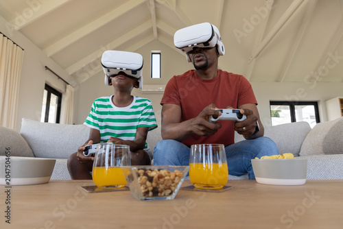 Cuadro en lienzo Father and son sitting on light sofa in living room wearing white VR headsets ho