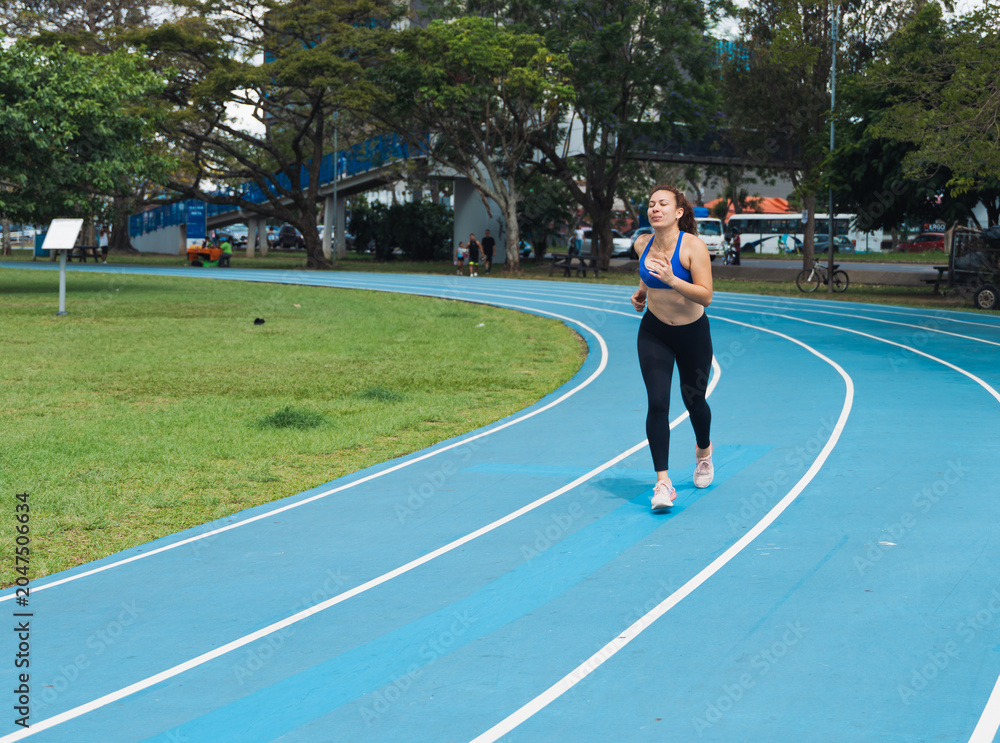 Fototapeta premium Woman running on blue athletic track during workout
