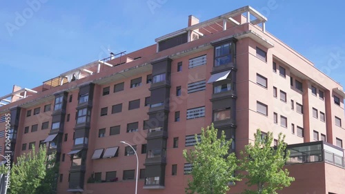 Modern residential apartment building featuring terracotta facade, balconies and contemporary urban housing architecture. Exterior view of multi-story residential development on a sunny day.