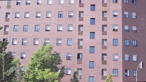 Modern red brick residential apartment building facade with repetitive window pattern and contemporary urban housing design. Exterior architectural view on a sunny day.
