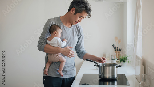 日本人父親が赤ちゃんを抱きながら台所で料理する写真