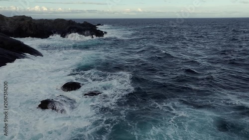 Waves crashing on jagged volcanic rocks along a moody coastline