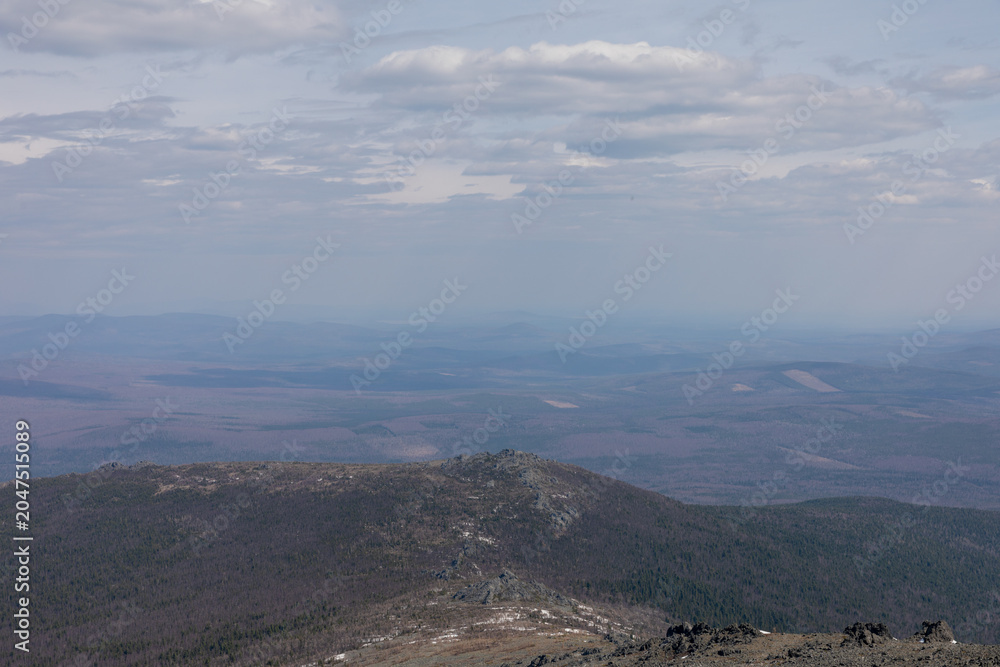 Obraz premium Wide panoramic landscape view from Konzhakovsky Stone in the Northern Urals, Sverdlovsk Oblast, Russia, with forested hills, rocky ridge and clouds