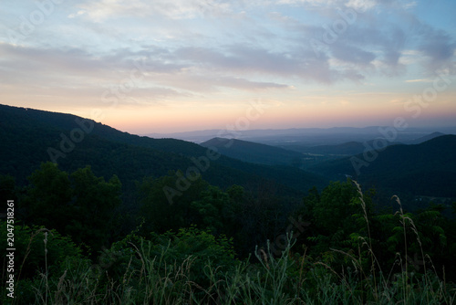 Clouds in the distance foliage in the foreground as the sun rises at Loft Mountain overlook