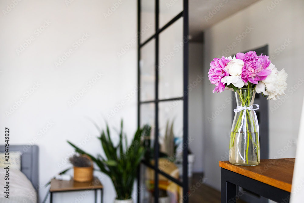 Fototapeta premium Pink and white peonies in a vase on a wooden table for a cozy home interior design or lifestyle blog decoration concept