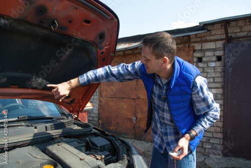 Cuadro en lienzo Man pointing at the engine under an open hood of an orange car in a garage driveway, checking problem, auto repair, vehicle maintenance, diy service