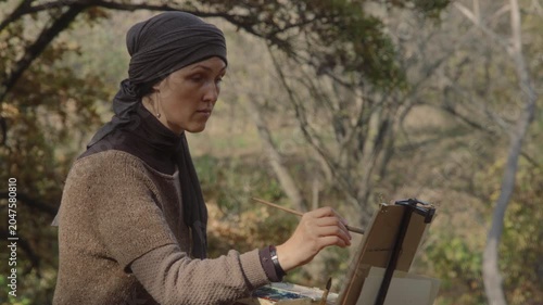 The artist paints a watercolor landscape in an autumn forest
