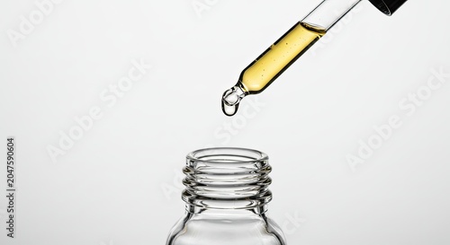 A dropper pours a yellow liquid into an empty glass bottle on a table indoors.