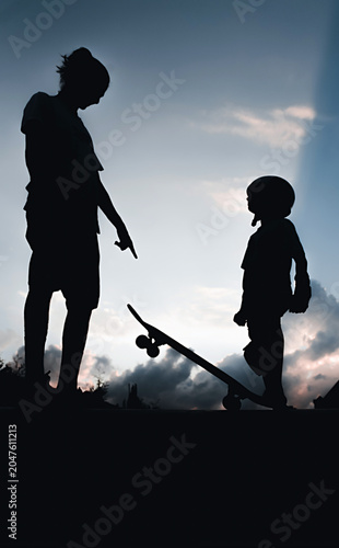 Silhouettes of people with a skateboard against the backdrop of a sunset, rays of sun breaking through the clouds