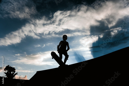 Silhouettes of people with a skateboard against the backdrop of a sunset, rays of sun breaking through the clouds