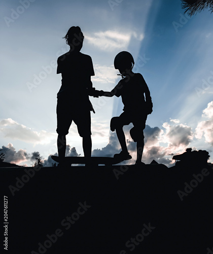 Silhouettes of people with a skateboard against the backdrop of a sunset, rays of sun breaking through the clouds