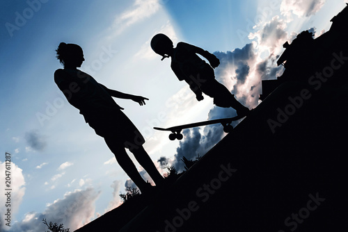 Silhouettes of people with a skateboard against the backdrop of a sunset, rays of sun breaking through the clouds