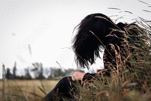 A girl sits in a field near a tree on green grass and paints a head with an orange fox sitting on it with watercolors on parchment paper