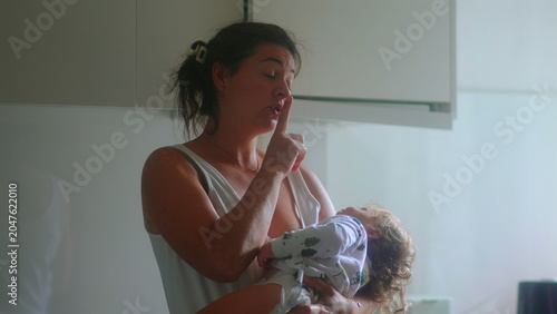 Fotografie Mother asking toddler to be quiet while holding child in kitchen capturing paren