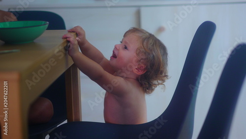 Foto Upset toddler beside dining chair during family mealtime needing help and suppor