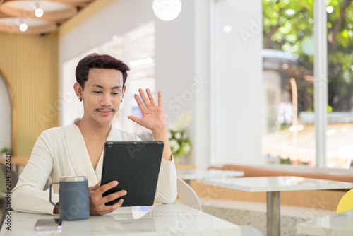 Bild auf Leinwand Non-binary gay Thai man waving at digital tablet during video call at a modern c