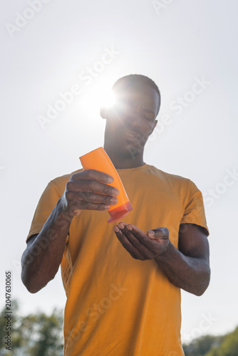Man stands outside on a sunny day, applying sunscreen lotion to protect his skin from UV rays during outdoor activities.