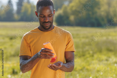 Man applies sunscreen lotion on a sunny summer day while enjoying outdoor activities for skin safety and sun protection.