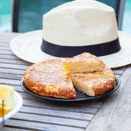 Spanish potato omelet on a wooden table with a summer hat.