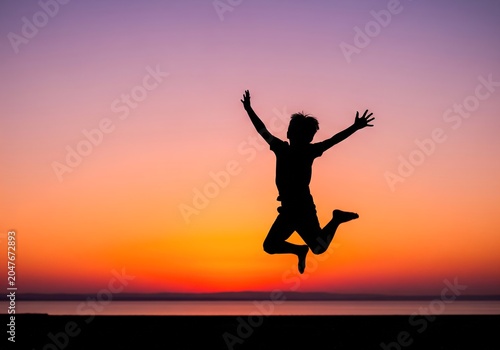 Boy Jumping for Joy Silhouette Against Colorful Sunset Sky Over Ocean Horizon
