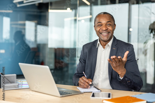 Foto Mature businessman laughing and gesticulating while sitting at a desk with a lap