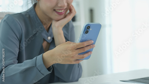 A smiling person looks at their smartphone while resting in a bright office.