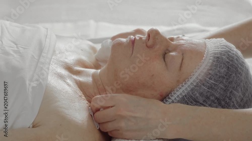 Cosmetologist wipes the face of an elderly woman with napkins before rejuvenating procedures