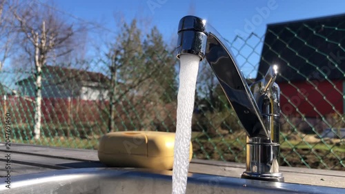 outdoor sink with a working faucet, a thin stream of clean water pouring out of it, a soap dish nearby, a blurred background, this is a scene of country life on a sunny day, loop